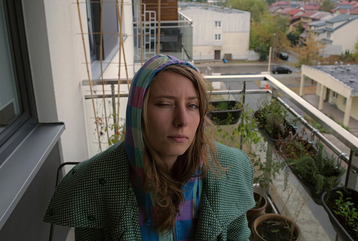 kobieta w wieku 30 plus siedzi na balkonie w płaszczu i kapturze z przymrużonym okiem