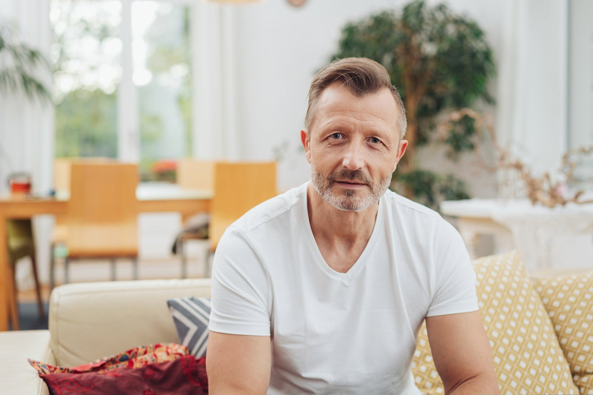 mężczyzna w wieku 45 plus w białym t-shircie siedzi na kanapie zamyślony