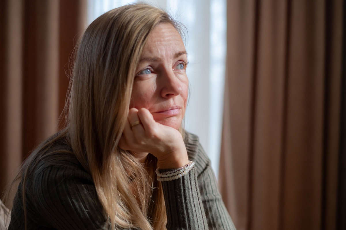 kobieta w wieku 40 plus blondynka z długimi włosami siedzi na tle okna zmartwiona, zamyślona i smutna