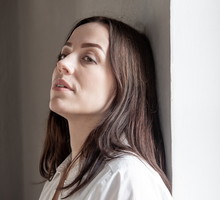 kobieta w wieku 35 plus z ciemnymi włosami stoi oaprta o scianę zamyślona