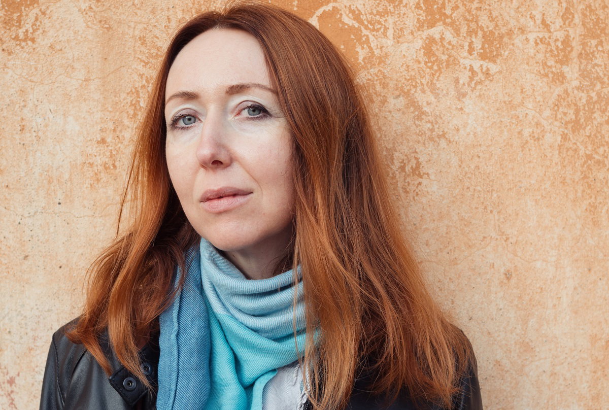 kobieta w wieku 40 plus z rudymi włosami pozuje na tle ściany w Olbii na Sardynii