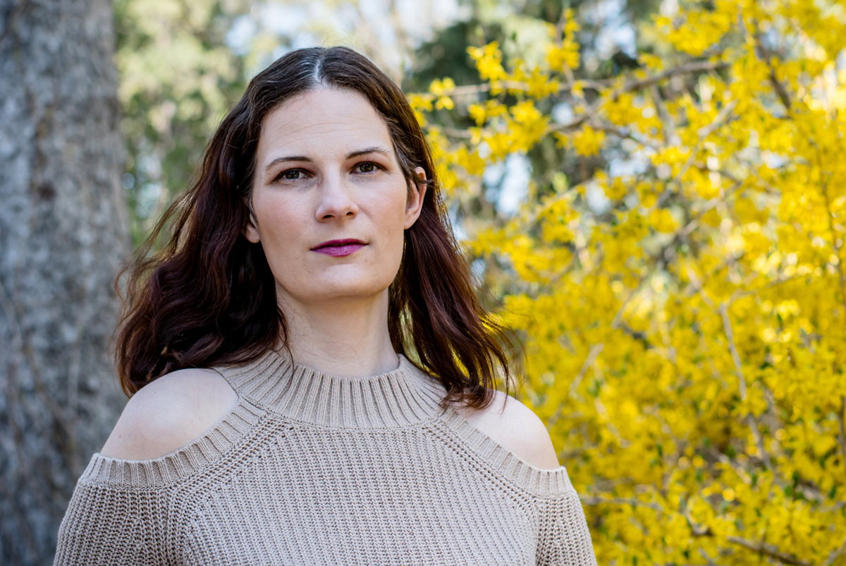 kobieta w wieku 35 plus w beżowym swetrze stoi na tle żółtych krzewów zamyślona