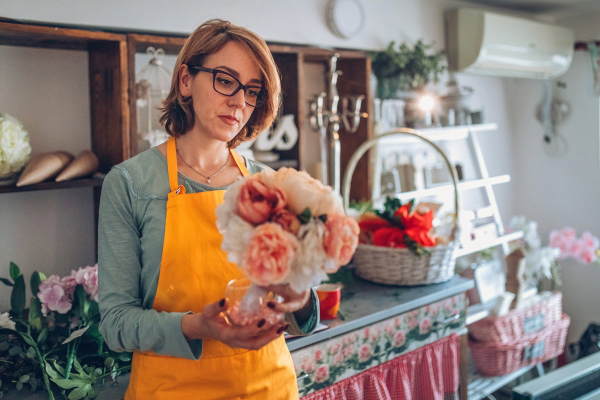 kobieta w wieku 30 plus w żółtym fartuszku trzyma bukiet stojąc w kwiaciarni