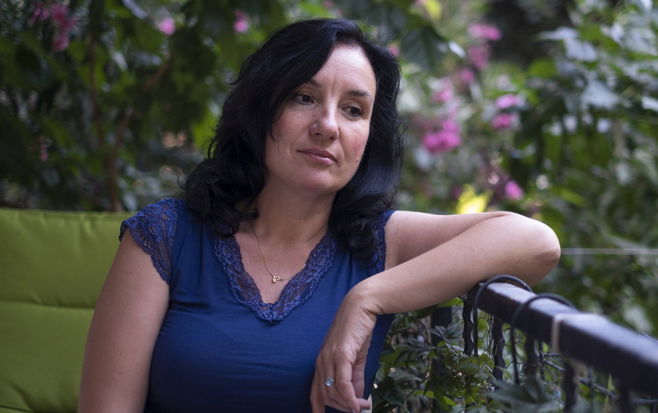 kobieta w wieku 50 plus ciemne włosy w niebieskiej bluzce siedzi na balkonie zamyślona