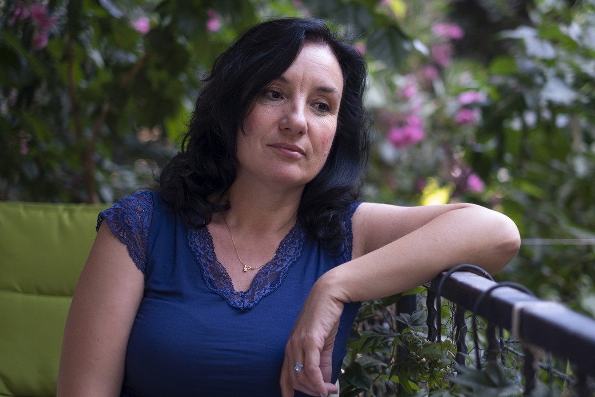 kobieta w wieku 50 plus ciemne włosy w niebieskiej bluzce siedzi na balkonie zamyślona