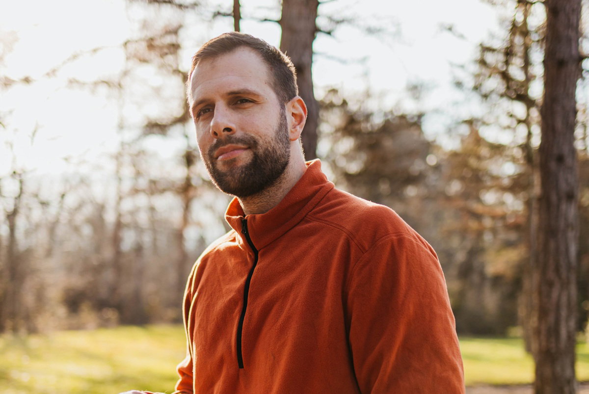 mężczyzna w wieku 35 plus w polarowej bluzie stoi na tle słonecznego lasu rozmarzony
