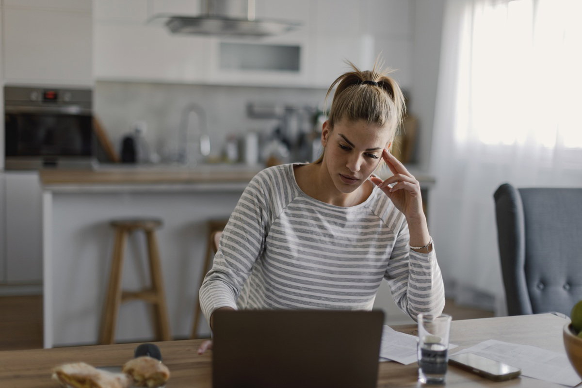 kobieta w wieku 25 plus blondynka siedzi przy laptopie w kuchni zasępiona