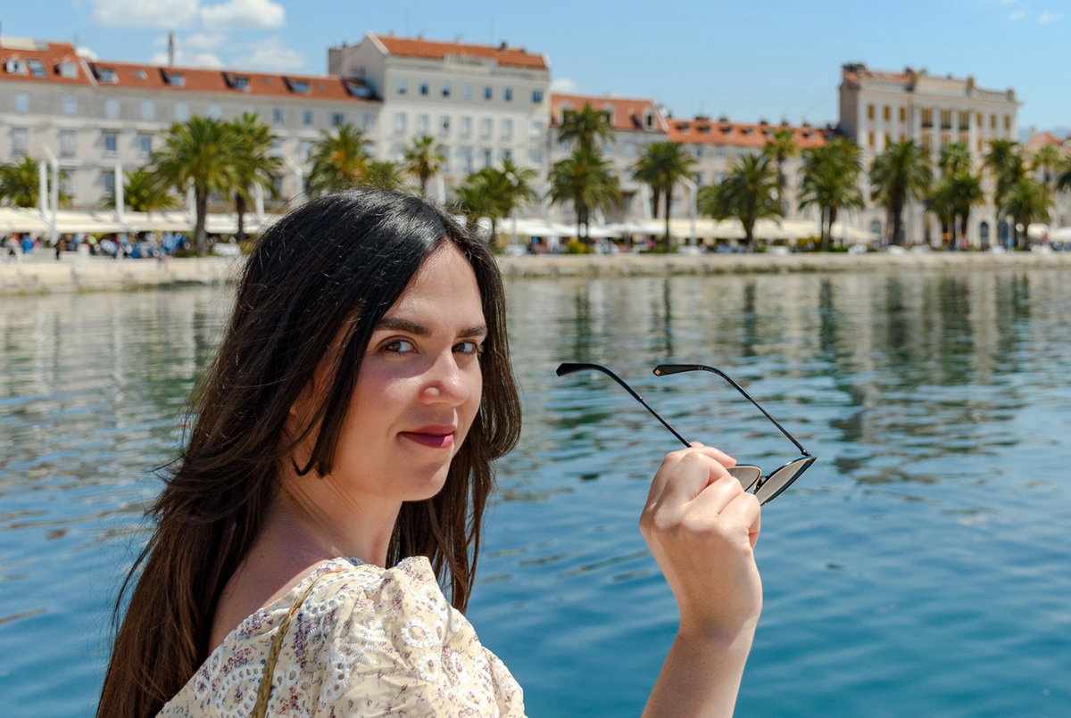 kobieta w wieku 30 plus z długimi włosami stoi na tle Splitu w Chorwacji z lekkim uśmiechem