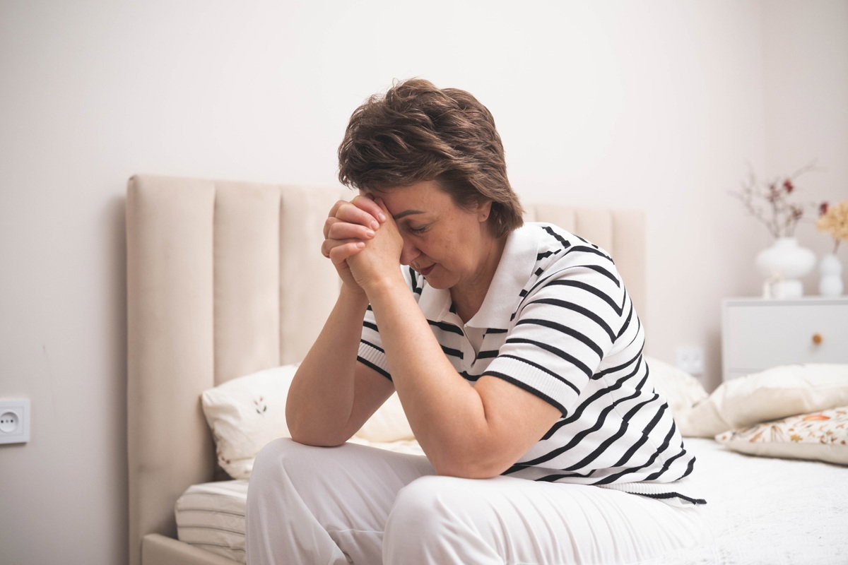 kobieta w wieku 50 plus w koszulce polo w paski siedzi w sypialni załamana