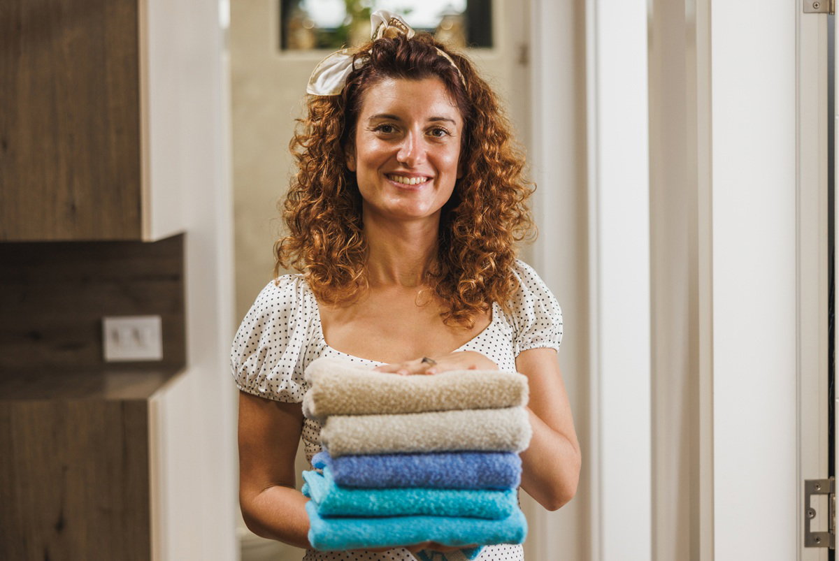 kobieta w wieku 35 plus stoi w korytarzu z wypranymi ręcznikami i się uśmiecha