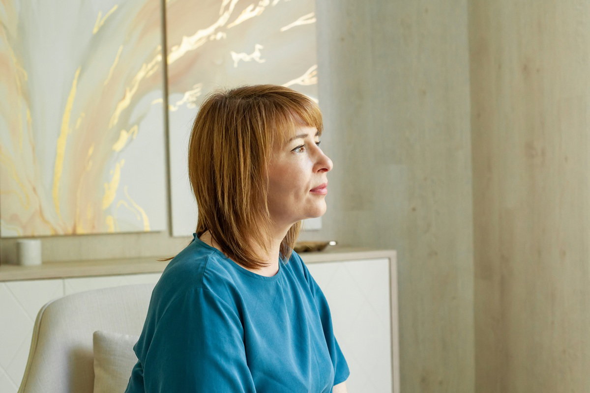 kobieta w wieku 45 plus w niebieskiej sukience siedzi w jasnym salonie zamyślona