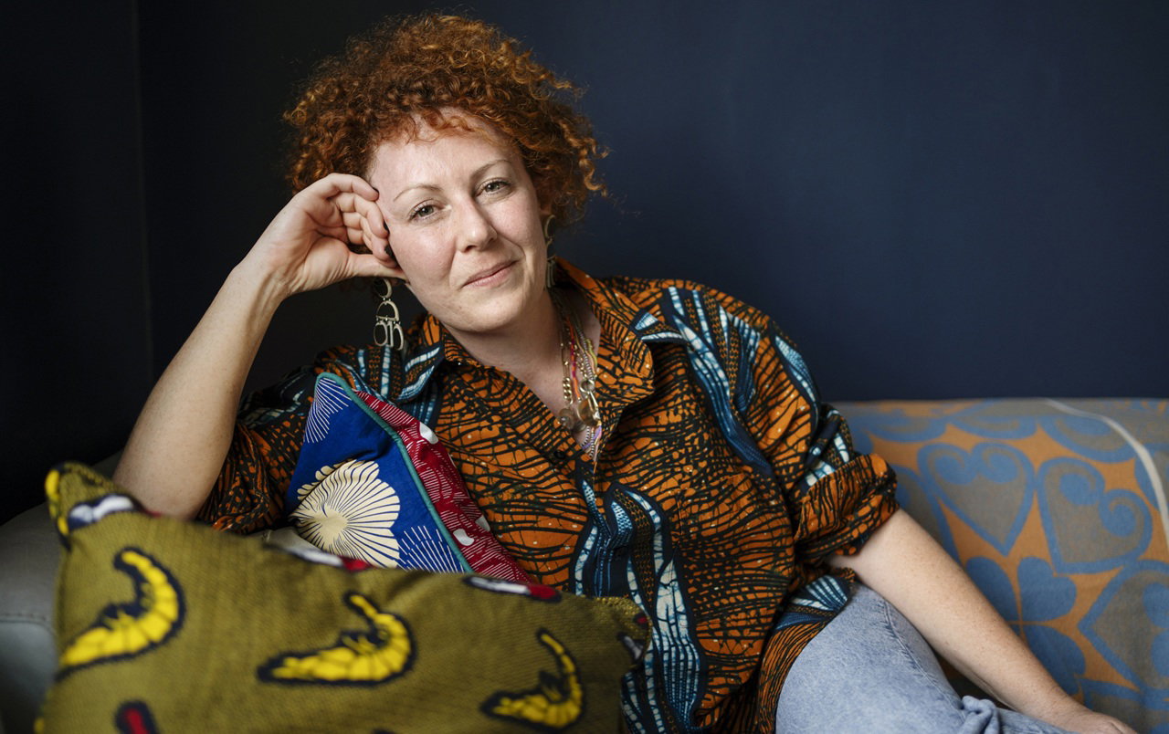 kobieta w wieku 40 plus we wzorzystej koszuli siedzi na wzorzystej kanapie z pewnym siebie lekkim uśmieszkiem