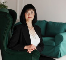 kobieta w wieku 35 plus siedzi w zielonym fotelu w luksusowym salonie z lekkim dumnym uśmiechem