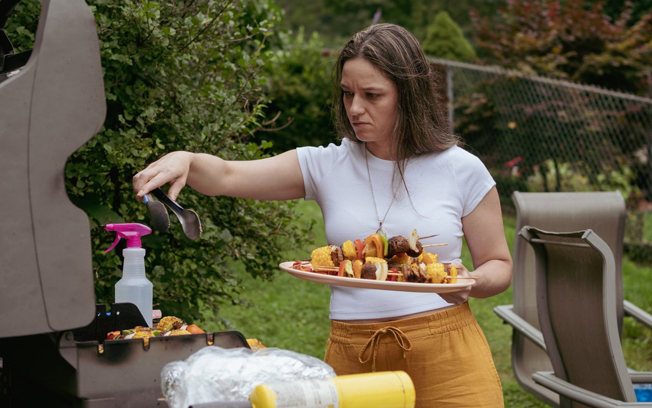kobieta w wieku 35 plus wyjmuje z grilla szaszłyki smutna i zamyślona