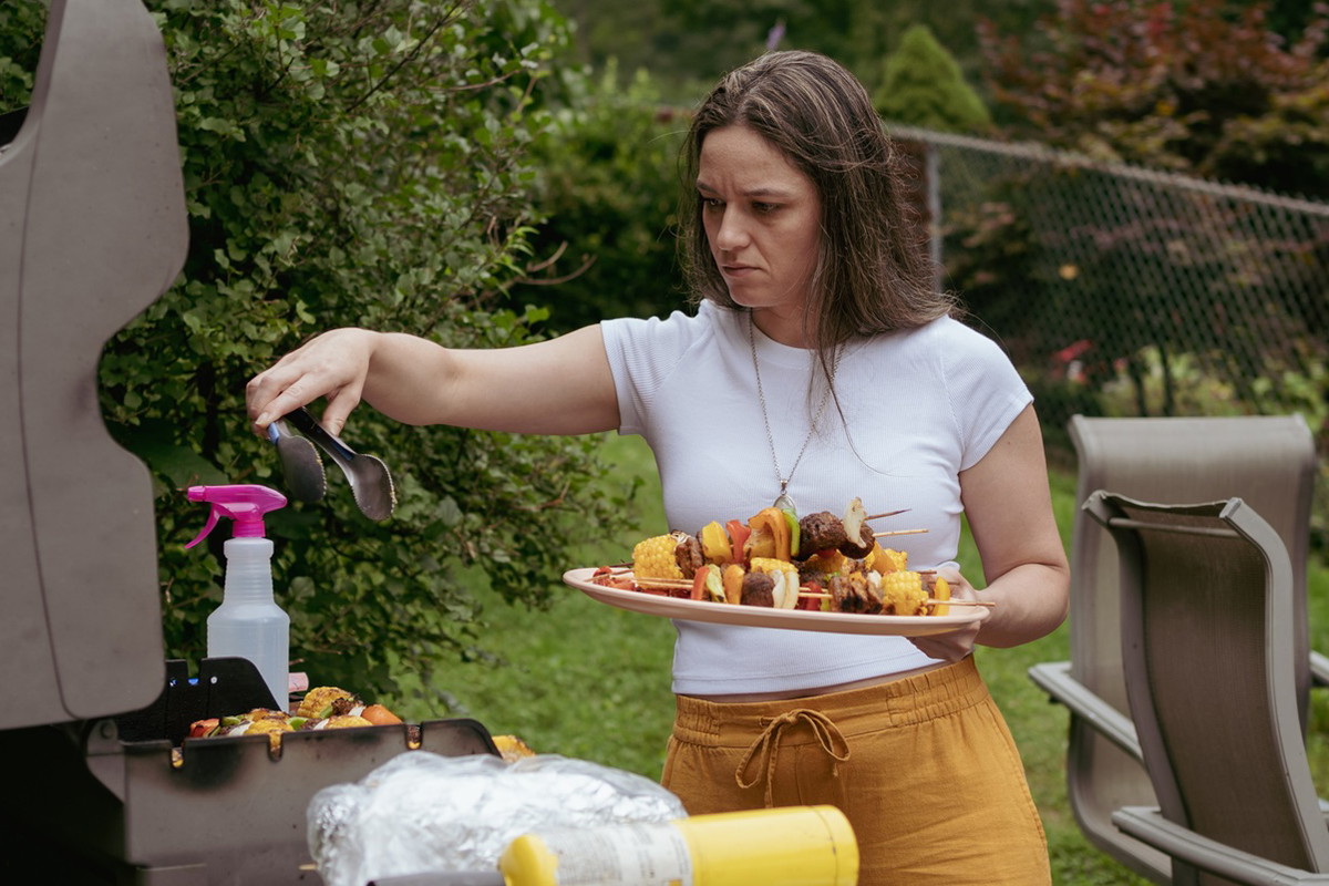 kobieta w wieku 35 plus wyjmuje z grilla szaszłyki smutna i zamyślona