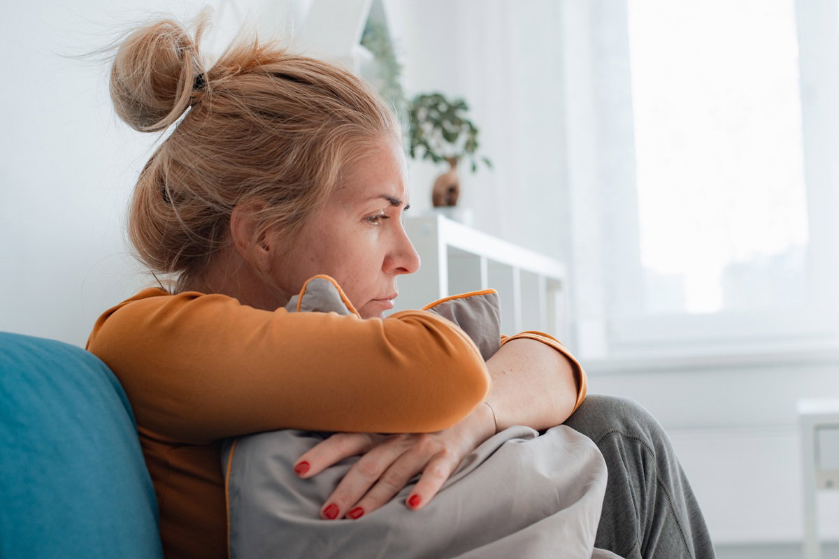 kobieta w wieku 40 plus blondynka w żółtej bluzce siedzi na kanapie załamana