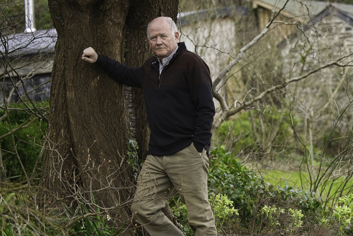 mężczyzna w wieku 60 plus opiera się o drzewo w ogrodzie ze smutną miną