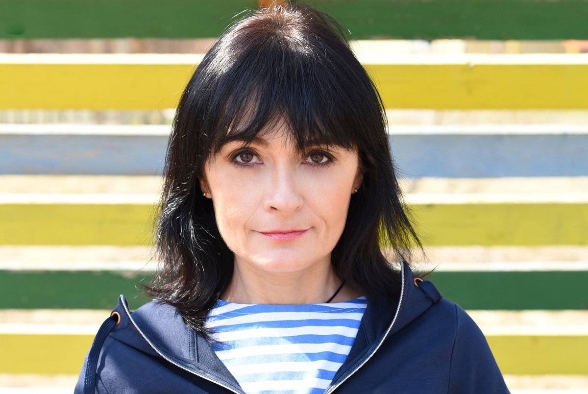 kobieta w wieku 40 plus z czarnymi włosami stoi na tle kolorowego płotu ze zdegustowaną miną