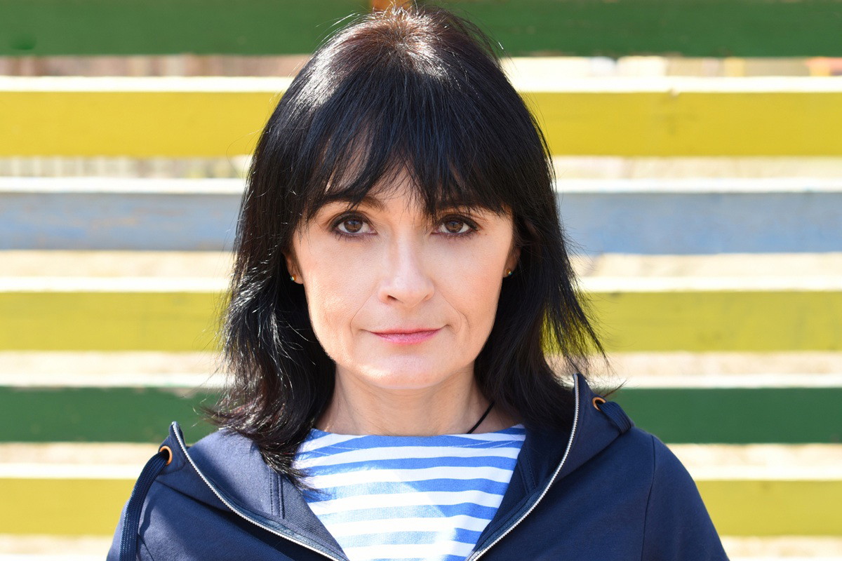 kobieta w wieku 40 plus z czarnymi włosami stoi na tle kolorowego płotu ze zdegustowaną miną