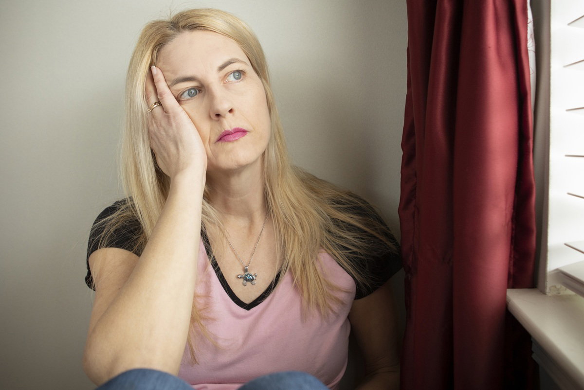 kobieta w wieku 40 plus blondynka siedzi przy oknie smutna i zamyślona
