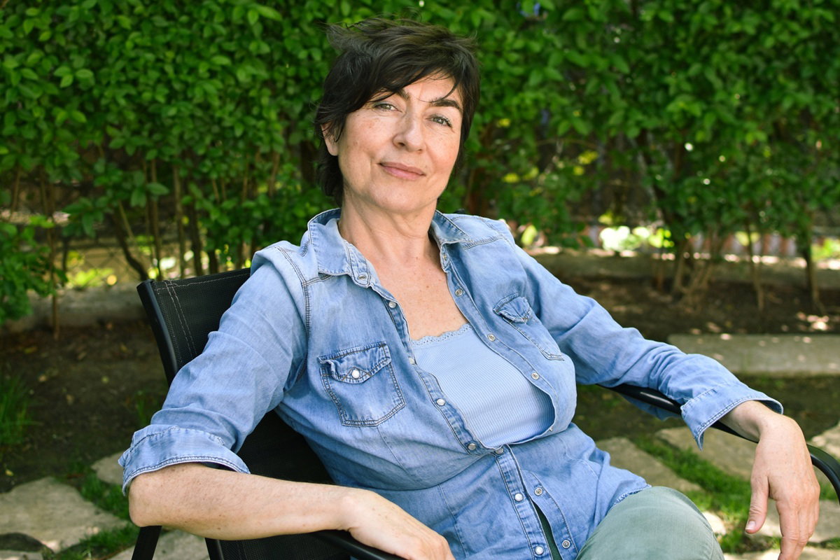 kobieta w wieku 50 plus siedzi na tle zieleni w ogrodzie z zadowoloną miną