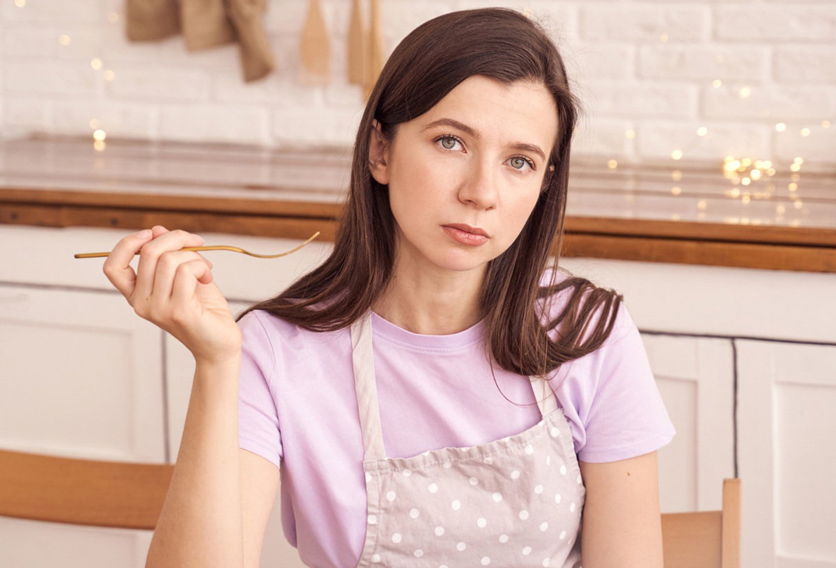 kobieta w wieku 30 plus siedzi w wysprzątanej kuchni smutna z widelcem w ręce