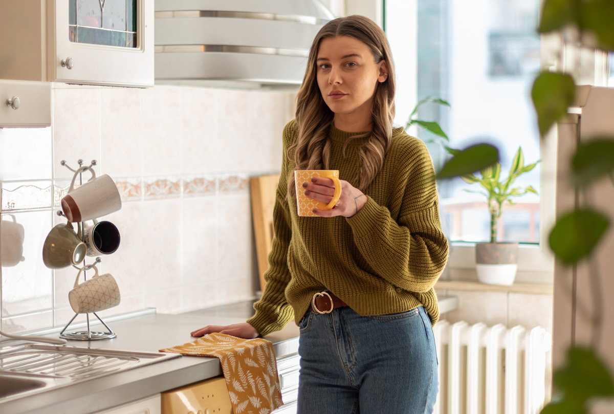 kobieta w wieku 25 plus długimi włosami stoi w kuchni z kubkiem zamyślona