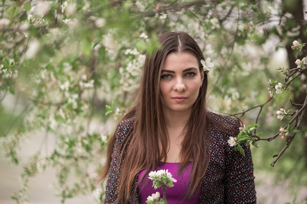 kobieta w wieku 25 plus z długimi włosami stoi wśród kwitnących drzew zamyślona