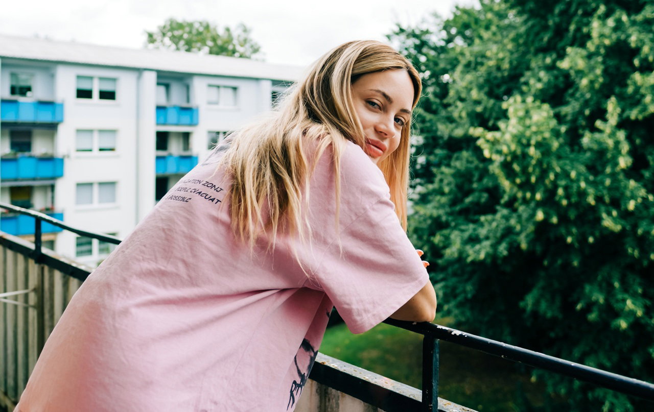kobieta w wieku 30 plus w różowym t-shircie blondynka stoi na balkonie i uśmiecha się lekko