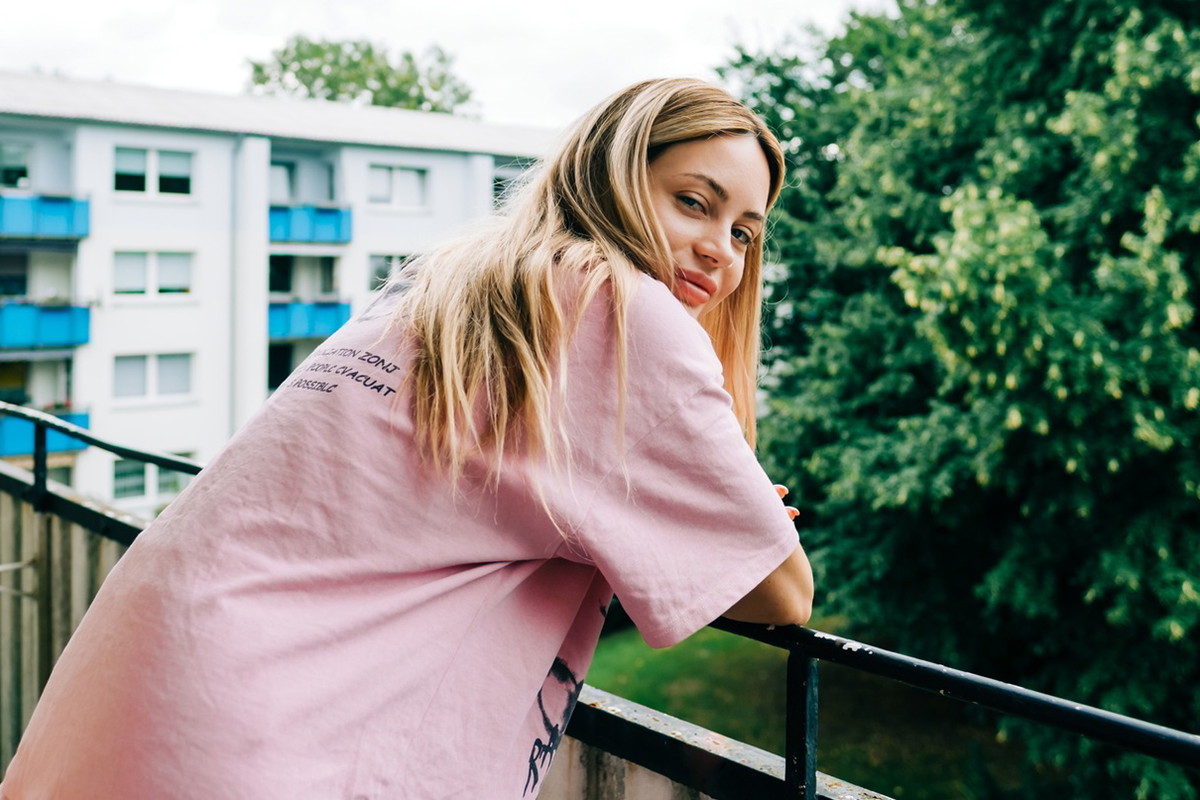 kobieta w wieku 30 plus w różowym t-shircie blondynka stoi na balkonie i uśmiecha się lekko