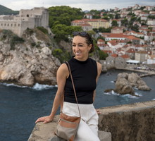 kobieta w wieku 30 plus stoi z torebką na tle Dubrovnika w Chorwacji i się uśmiecha