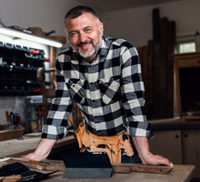 mężczyzna w wieku 40 plus w kraciastej koszuli stoi w warsztacie i się uśmiecha