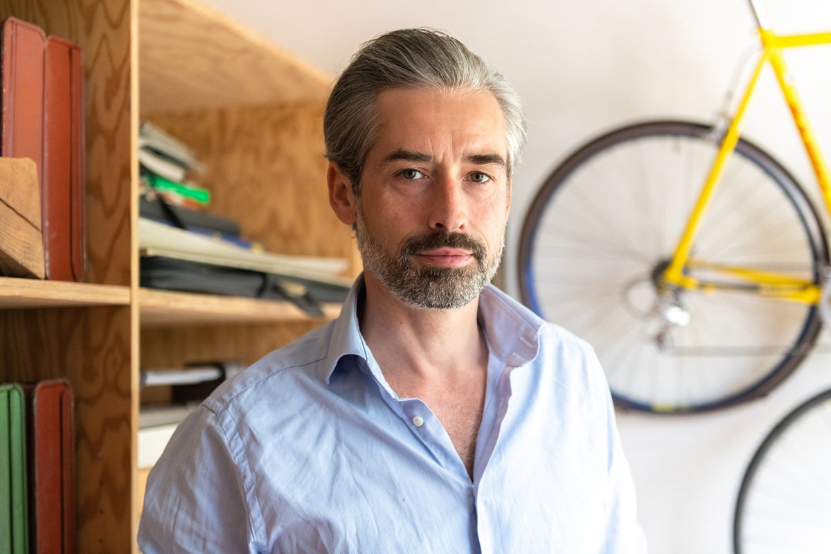 mężczyzna w wieku 45 plus siwiejący z zarostem w jasnej koszuli stoi w garażu smutny i zamyślony