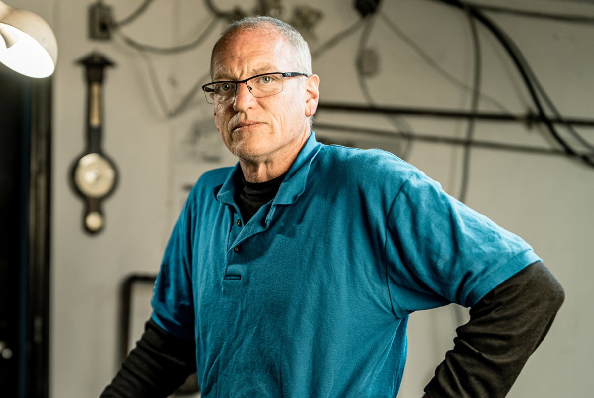 mężczyzna w wieku 45 plus w okularach łysiejący stoi na tle warsztatu ze smutną miną