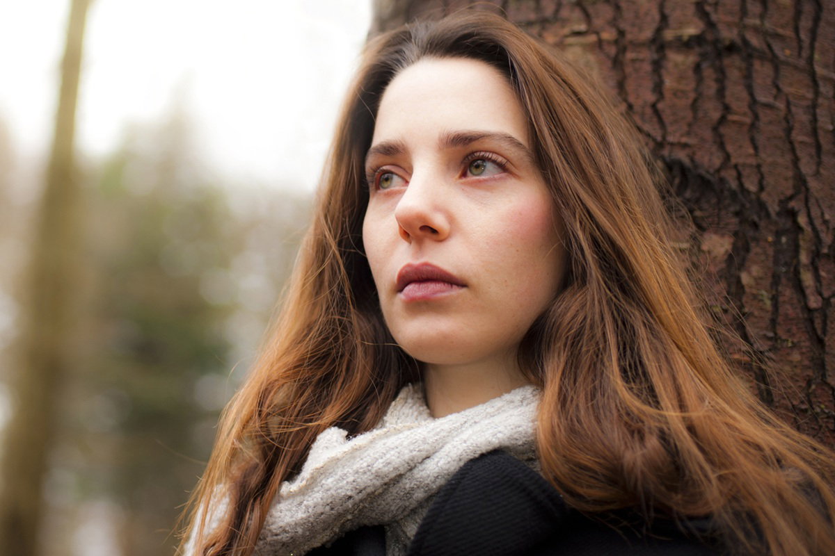 kobieta w wieku 25 plus z długimi włosami opiera się o drzewo smutna i zamyślona