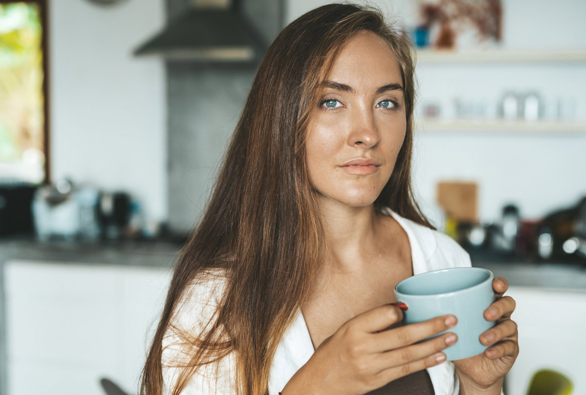 kobieta w wieku 30 plus stoi w kuchni z kubkiem w ręku zamyślona