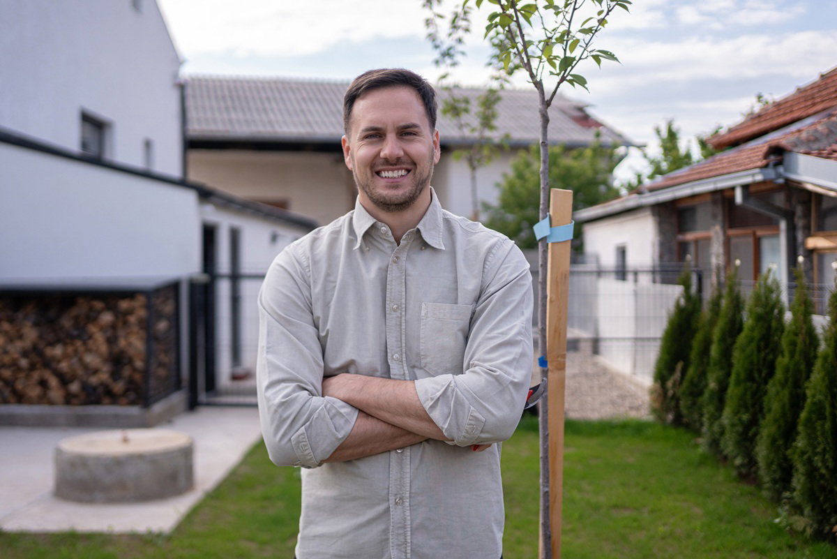 mężczyzna w wieku 30 plus stoi przy drzewku na ogródku i się uśmiecha