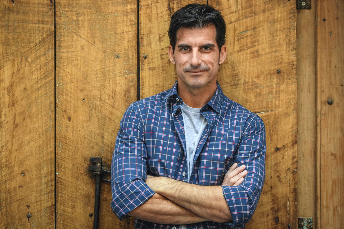 przystojny mężczyzna w wieku 40 plus stoi na tle drewnianych drzwi i uśmiecha się szelmowsko