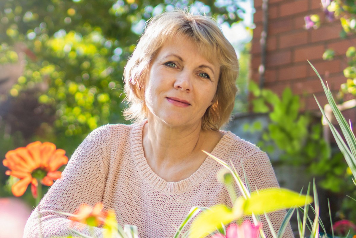 kobieta w wieku 50 plus blondynka w ogrodzie kuca rozmarzona