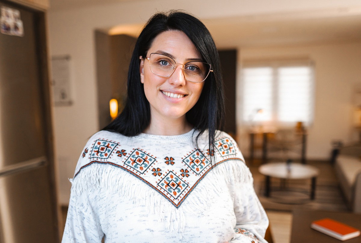 kobieta w wieku 30 plus w okularach z ciemnymi włosami stoi na tle kuchni i lekko się uśmiecha