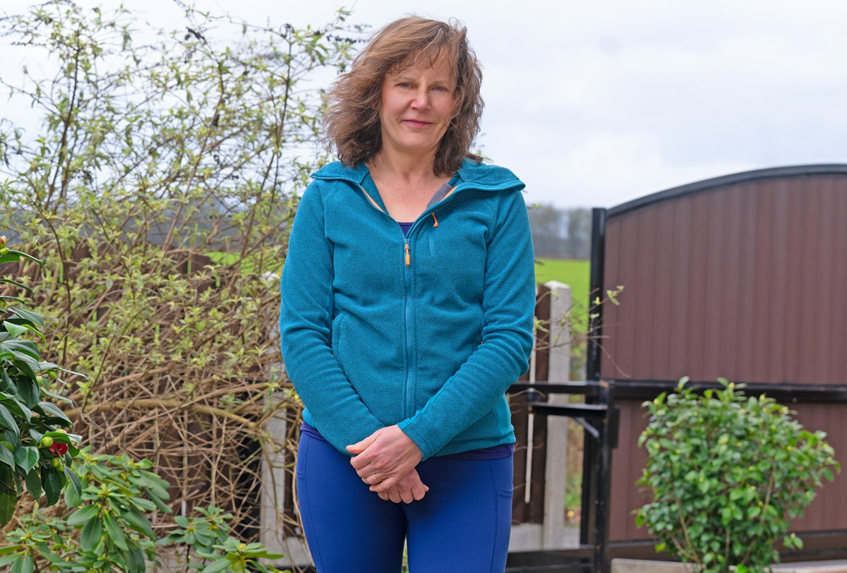 kobieta w wieku 55 plus w niebieskiej bluzie stoi w ogrodzie z niepewną miną