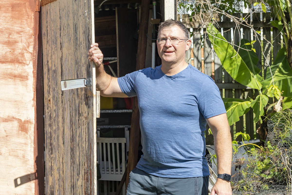 mężczyzna w wieku 50 plus w okularach stoi przy szopie ogrodowej z poważną miną