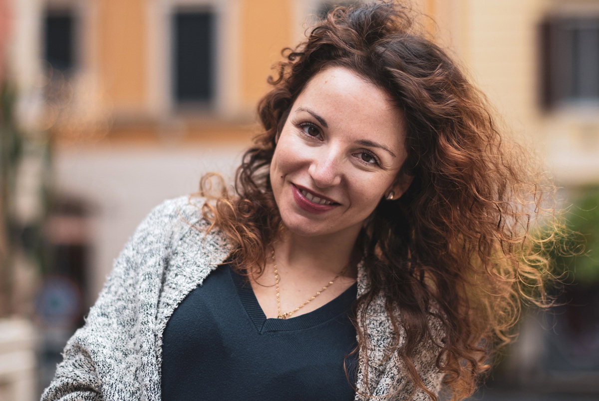 kobieta w wieku 35 plus z kręconymi włosami stoi na tle budynków we Włoszech uśmiechnięta