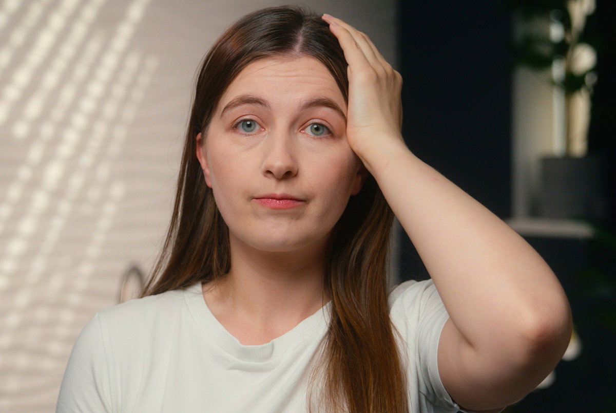 kobieta w wieku 35 plus w jasnym t-shircie zmartwiona patrzy ze smutkiem i trzyma się za głowę