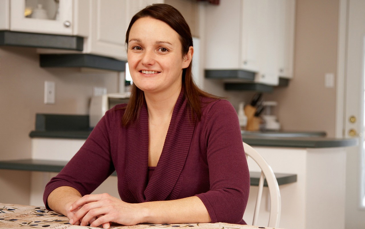 kobieta w wieku 30 plus w bordowym swetrze siedzi w kuchni przy stole i uśmiecha się nieśmiało