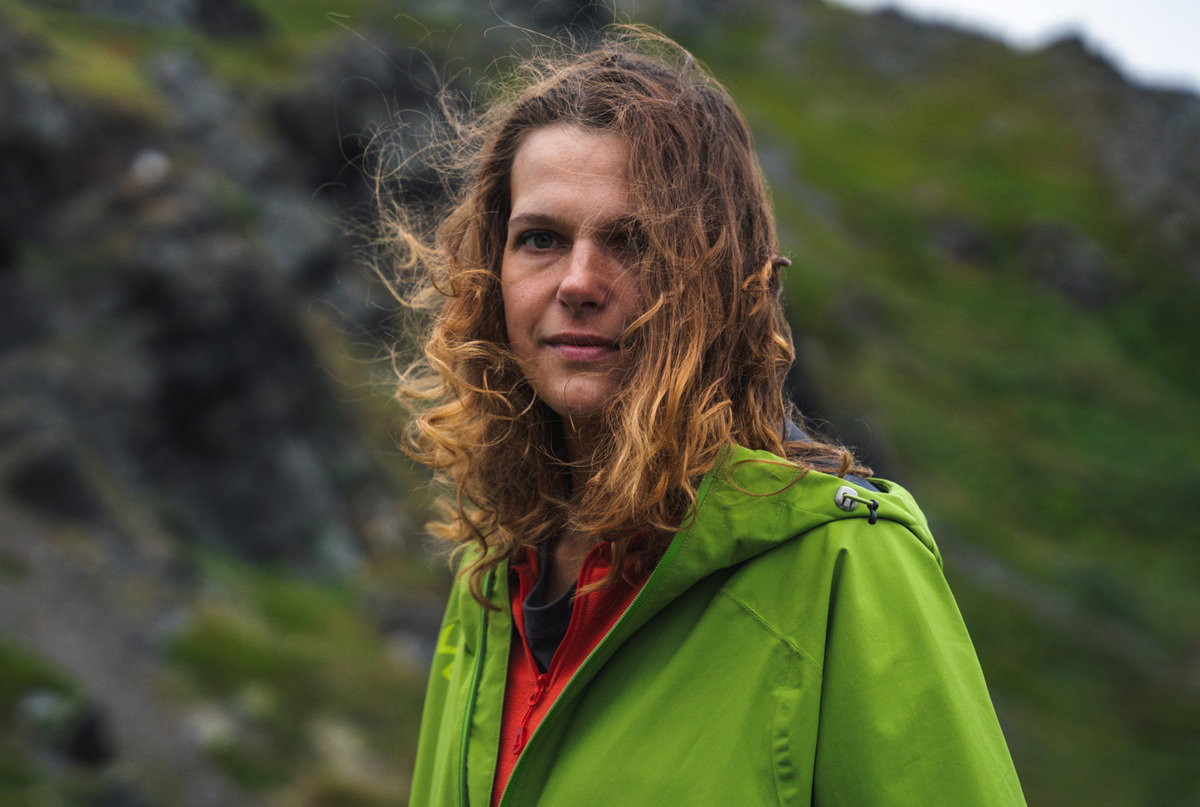 kobieta w wieku około 40 lat w zielonej kurtce stoi na tle górzystego pejzażu