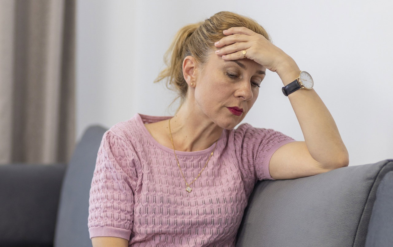 kobieta w wieku 40 plus w różowym ażurowym sweterku siedzi na kanapie załamana