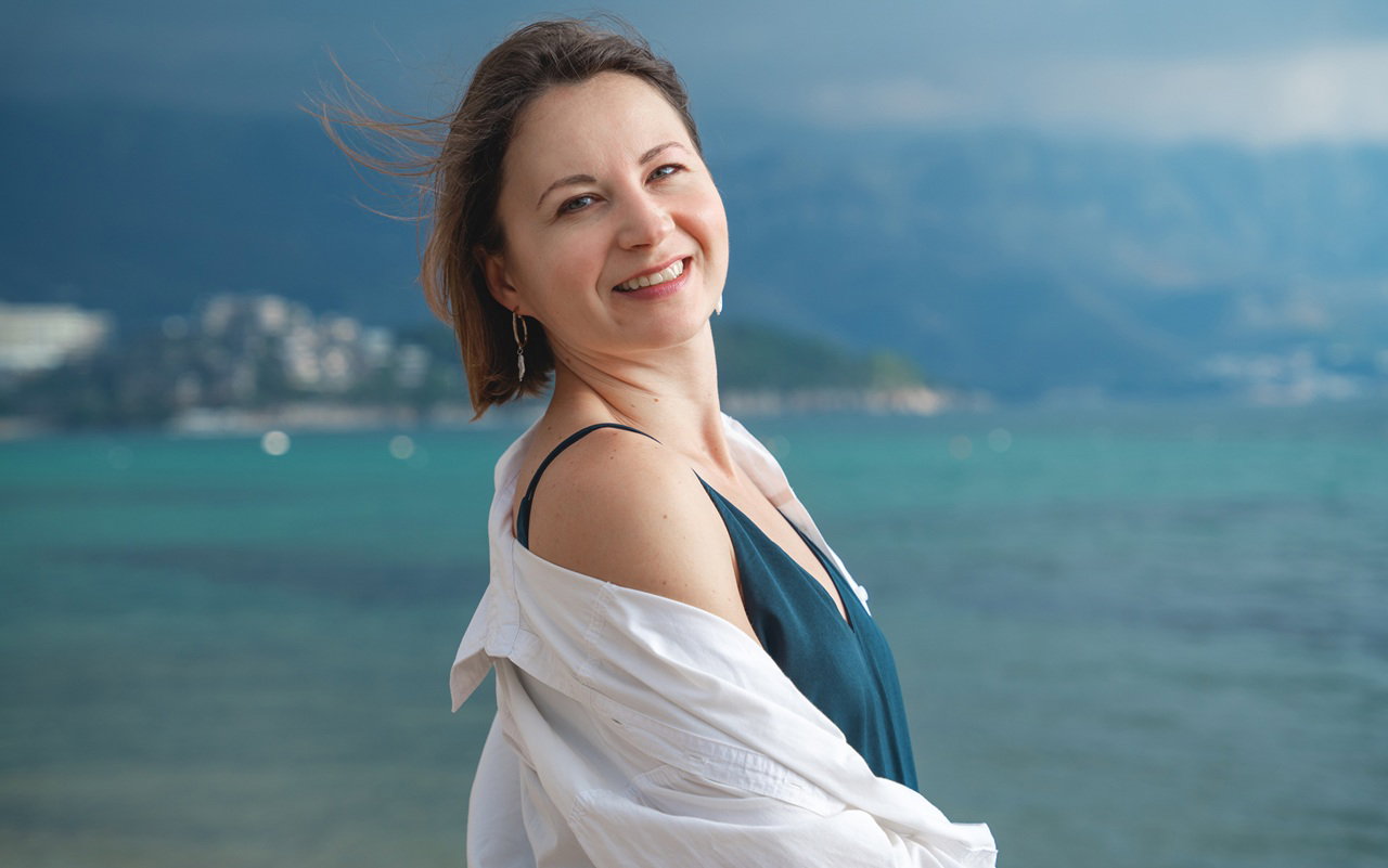 kobieta w wieku 40 plus stoi na tle wakacyjnego pejzażu i uśmiecha się napawając wolnością