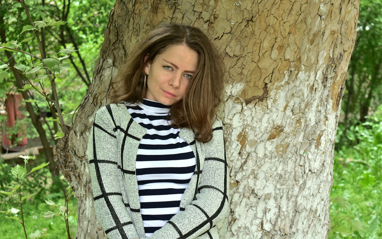 kobieta w wieku 35 plus z dziwnym spojrzeniem stoi na tle pnia dużego drzewa