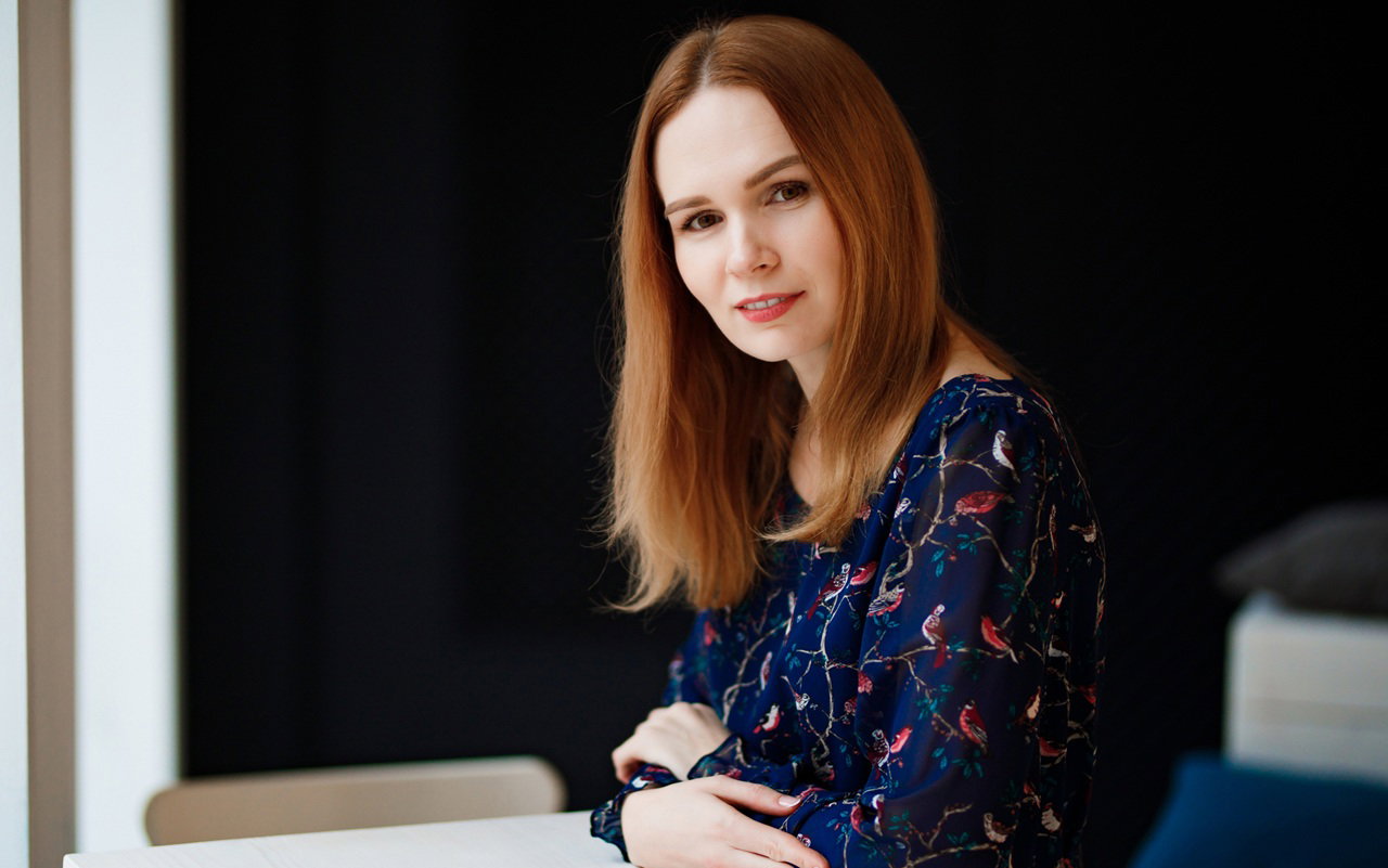 kobieta w wieku 30 plus z długimi włosami siedzi uśmiecha się z przekąsem na czarnym tle